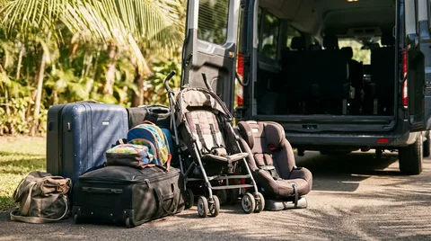 Luggage, stroller and child seat prepared beside the open compartment of an unbranded airport transfer van