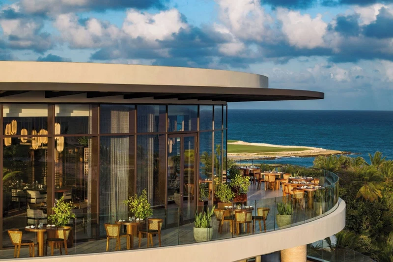 A modern building with a glass facade overlooking a beach and ocean.