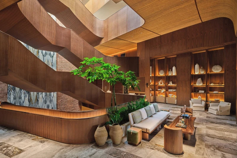 A modern lobby with a curved reception desk, a staircase, and a seating area with sofas and a coffee table.