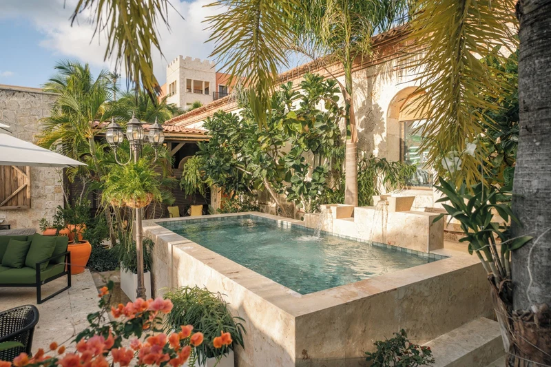 A swimming pool surrounded by lush greenery, stone walls, and outdoor furniture.