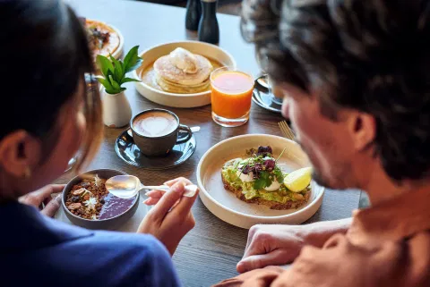 A dining table with breakfast items including pancakes, a cup of coffee, and a glass of orange juice.