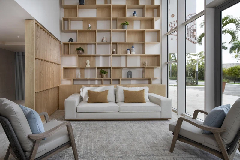 A modern living room with a white sofa, two armchairs, and a wooden shelving unit filled with decorative items.