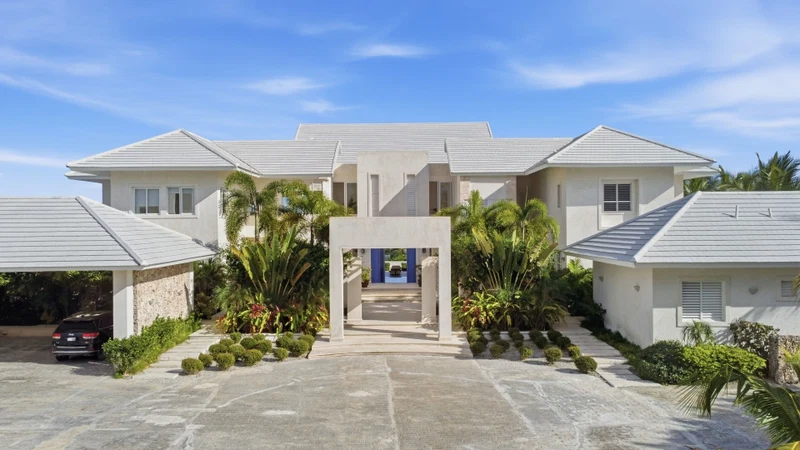A large, modern house with a central entrance, surrounded by well-maintained landscaping and a paved driveway.