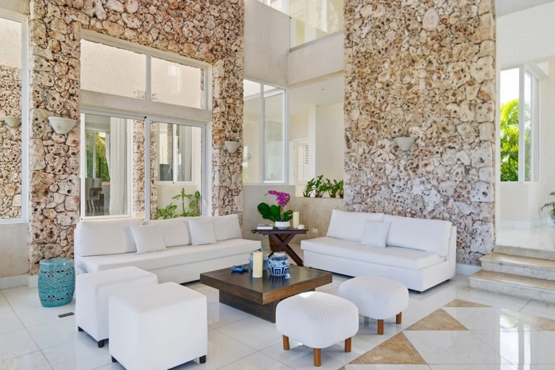 A modern living room with white sofas, a coffee table, and a stone accent wall.