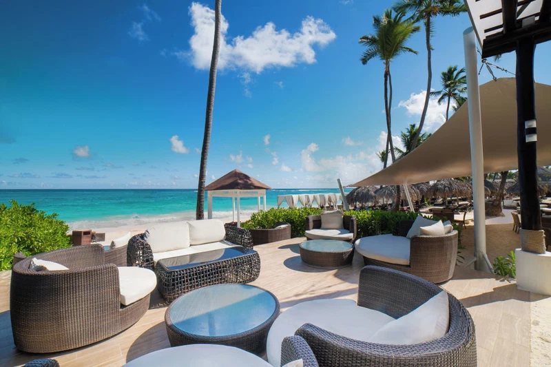 A beachside lounge with wicker furniture, a thatched-roof gazebo, and a view of the ocean.