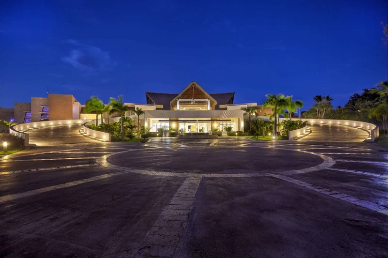 A hotel with a central entrance, a curved driveway, and palm trees.
