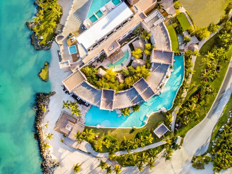 An aerial view of a resort with multiple swimming pools, a large building, and surrounding palm trees.