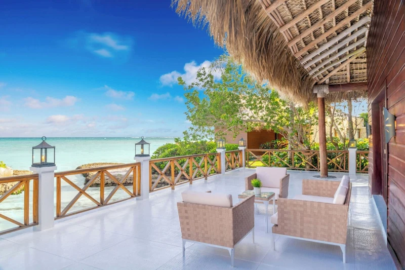 A seaside patio with wicker furniture, a thatched roof, and a view of the ocean.
