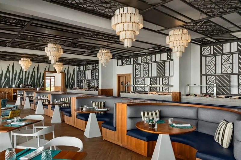 A modern restaurant with wooden tables, cushioned seating, and decorative chandeliers.