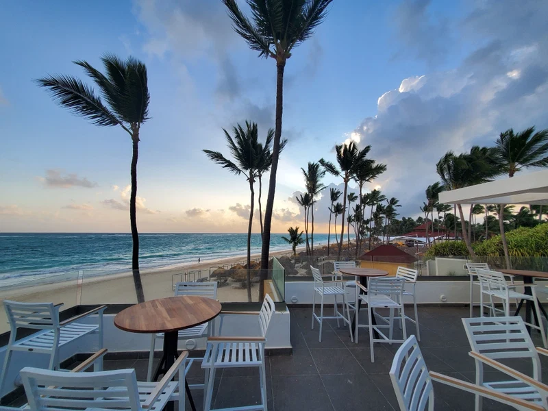 A beachside patio with white metal chairs and tables, overlooking the ocean.