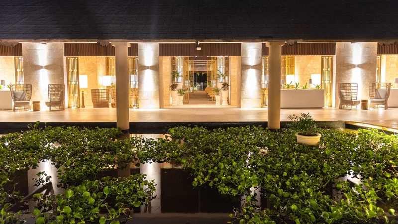 A hotel lobby with a reception desk, seating area, and a water feature with plants.