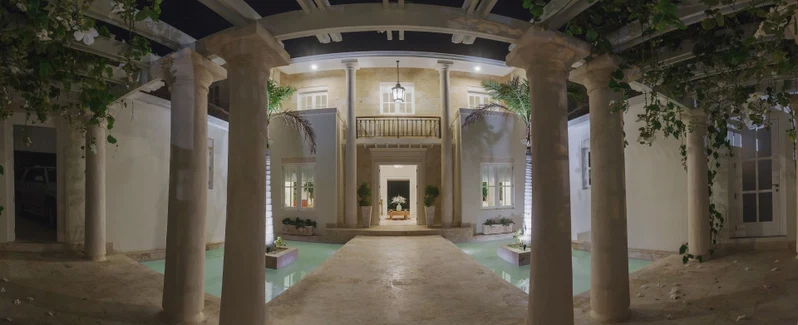 A covered walkway with columns, a central door, and potted plants.