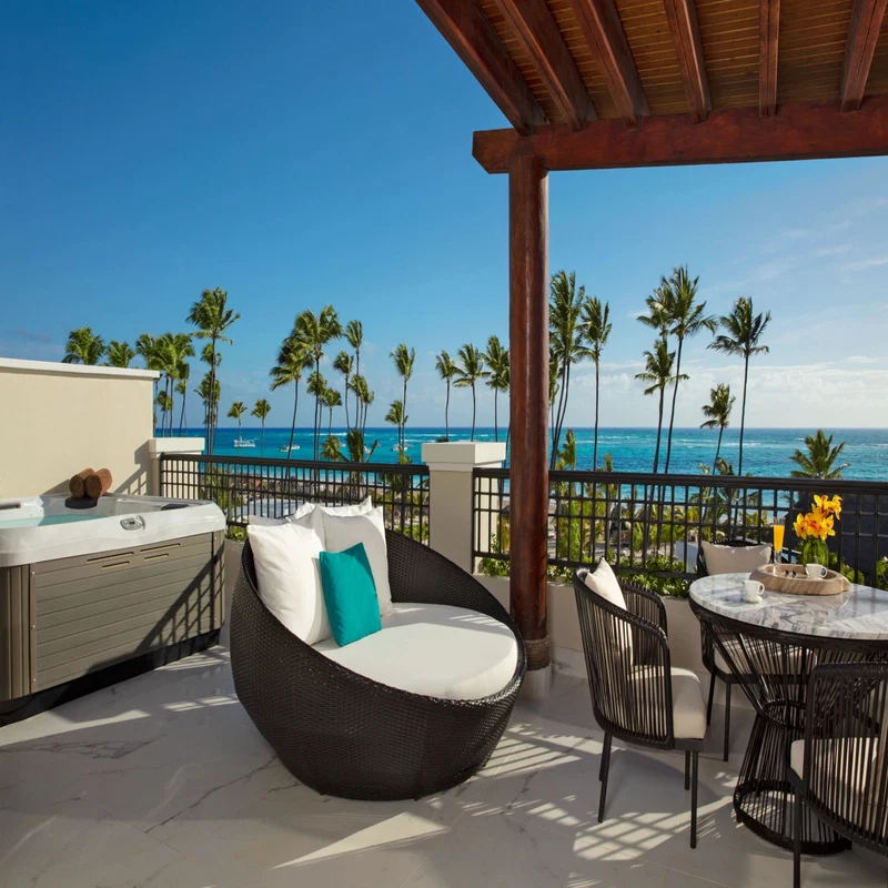 A balcony with a hot tub, wicker furniture, and a table with a vase of flowers.
