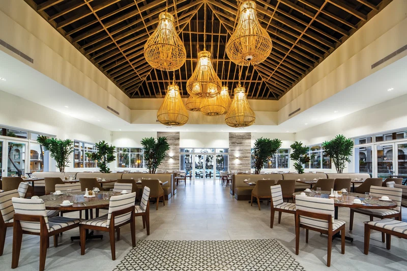 A spacious hotel lobby with multiple seating areas, a high ceiling with wooden beams, and hanging light fixtures.