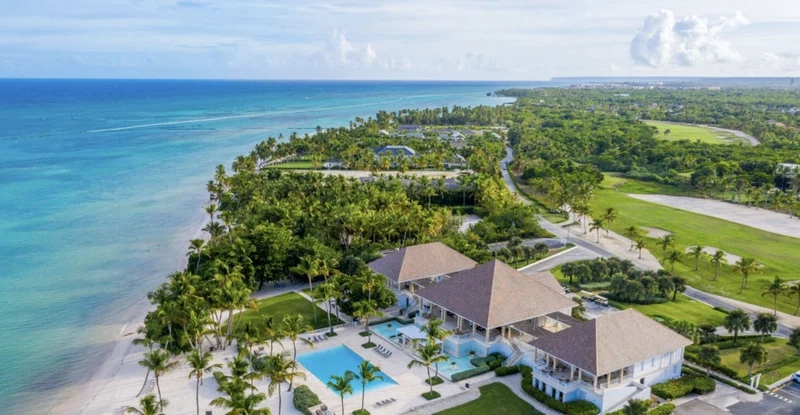 An aerial view of a resort with a large pool, beachfront, and lush greenery.