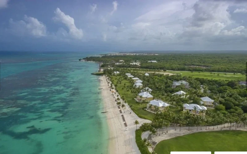 An aerial view of a coastal resort with a beachfront, lush greenery, and multiple villas.