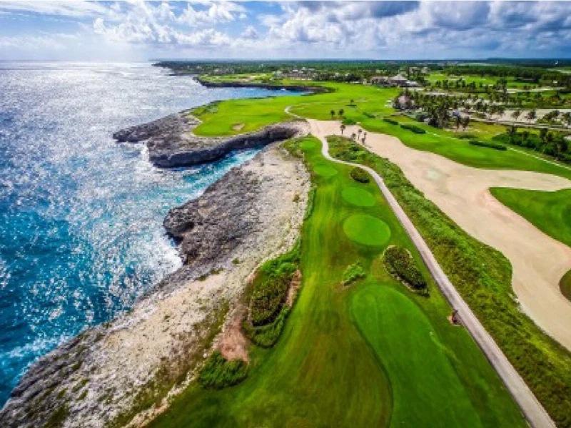 An aerial view of a coastal golf course with a clear path, green fairways, and a rocky shoreline.
