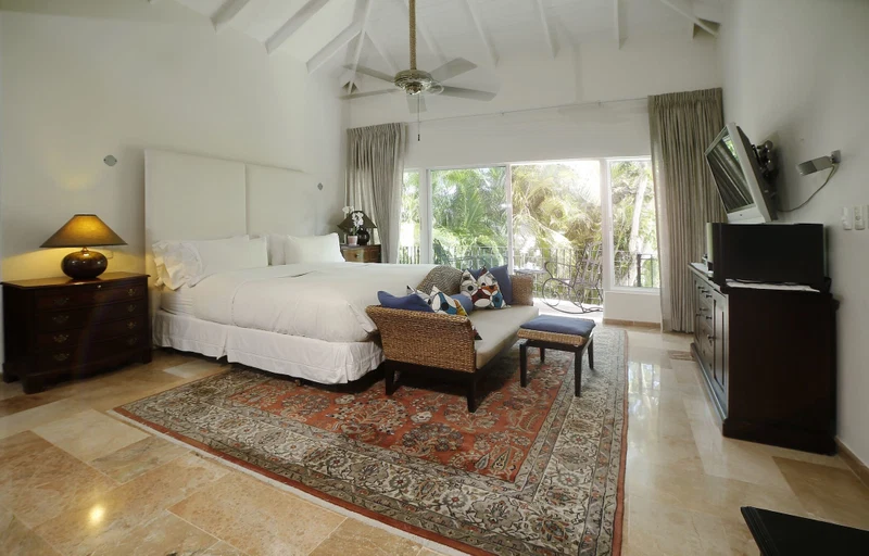 A bedroom with a bed, nightstand, lamp, dresser, TV, and a view of the outdoors.