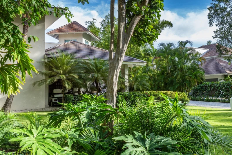 A modern house with a red-tiled roof, surrounded by lush greenery and palm trees.