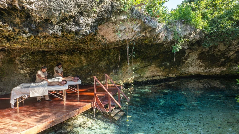 A spa area with wooden platforms and benches overlooking a clear blue pool.