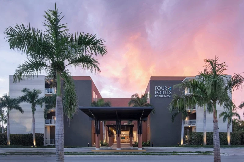 A hotel entrance with a covered walkway, palm trees, and a sign reading "FOUR POINTS BY SHEARERON".