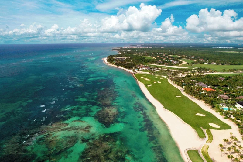 An aerial view of a coastal area with a golf course, beachfront, and residential buildings.