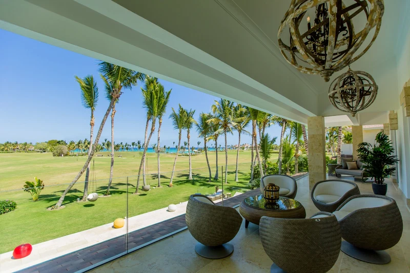 A spacious room with a view of a golf course and palm trees, furnished with modern chairs and a table.