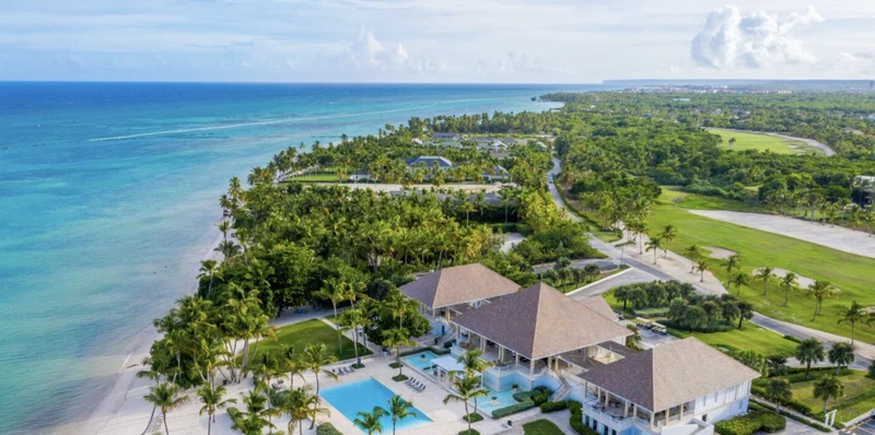 An aerial view of a resort with a large building, a swimming pool, and a beach.