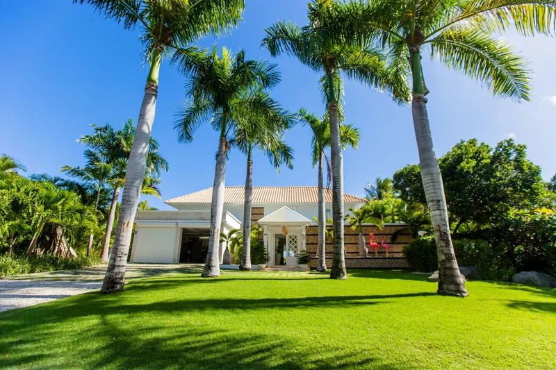 A house with a white exterior, a red-tiled roof, and a covered porch with palm trees in the foreground.