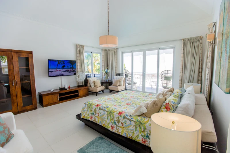 A spacious bedroom with a large bed, a TV, a balcony, and a wooden wardrobe.