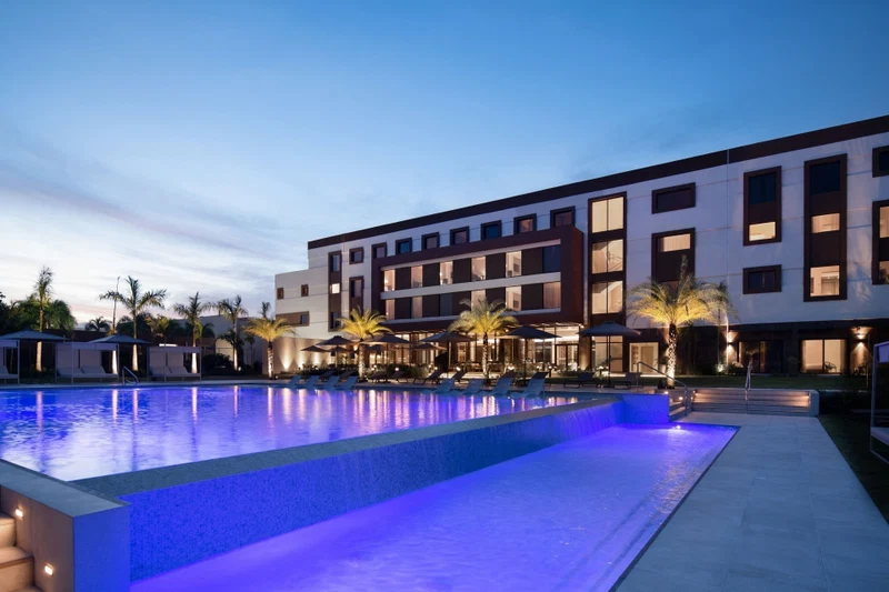 A modern hotel with a swimming pool, outdoor seating, and palm trees.