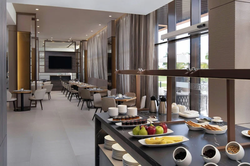 A modern dining area with a buffet setup, including fruits, pastries, and beverages.