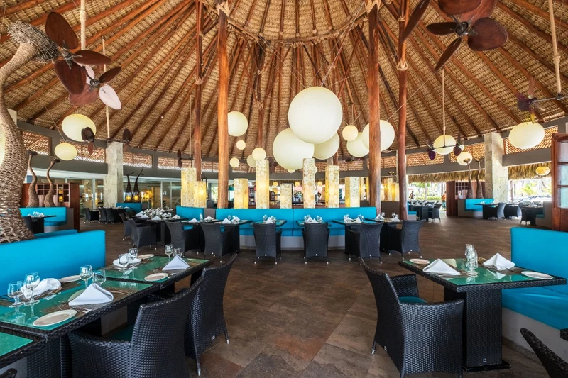 A spacious restaurant with high ceilings, hanging spherical lights, and blue upholstered seating.