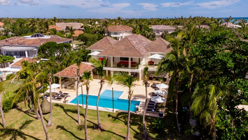 A large house with a swimming pool surrounded by palm trees and a view of the ocean.
