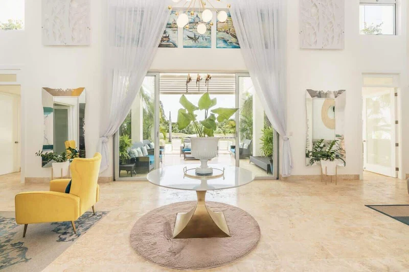 A spacious lobby with a round table, yellow armchairs, and a large window offering a view of the outdoors.