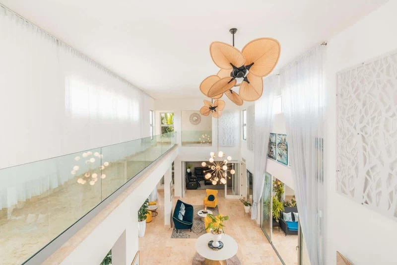 A spacious, modern interior with a high ceiling, a glass railing, and a central seating area with a round table and chairs.