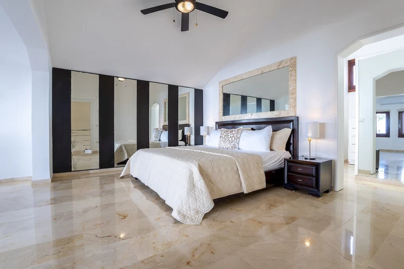A spacious bedroom with a large bed, a ceiling fan, a nightstand, and a mirror above the bed.