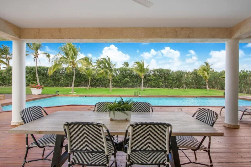 A covered outdoor area with a pool, dining table, and chairs.