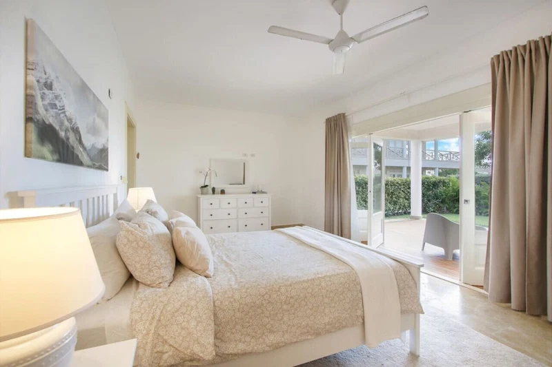 A bedroom with a bed, a nightstand, a dresser, a ceiling fan, and a sliding glass door to a balcony.