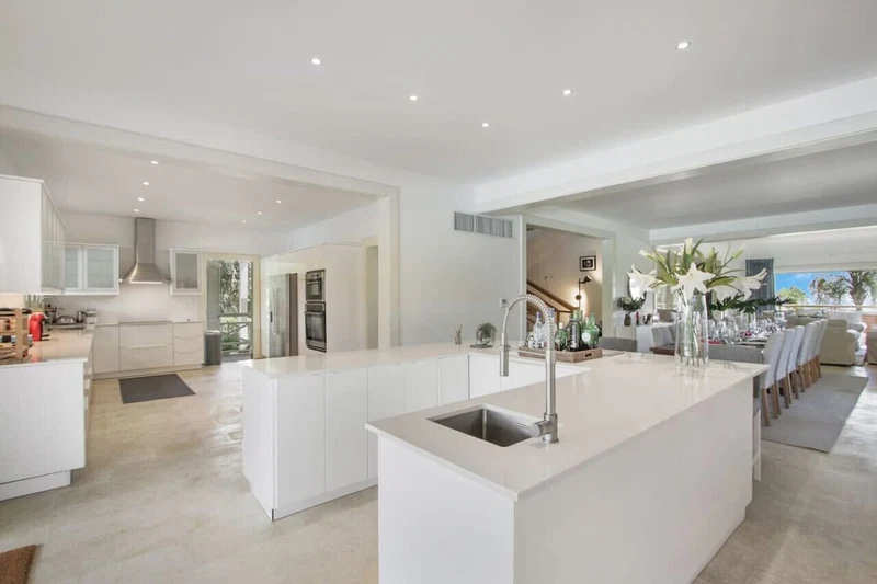 A modern kitchen with a large island, white cabinetry, and a dining area with a view.