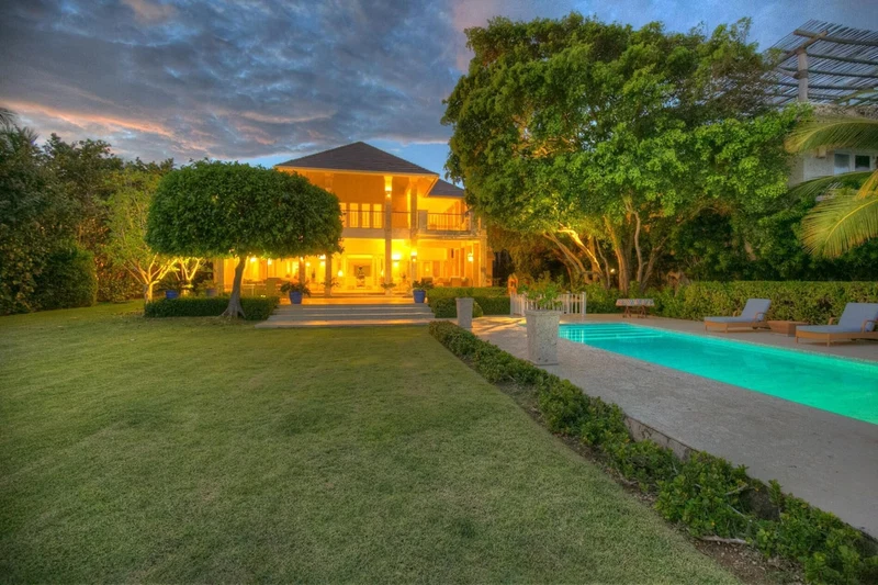 A two-story house with a swimming pool, surrounded by well-maintained lawns and trees.