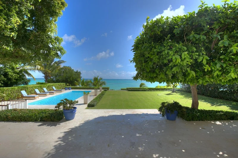 A pool area with lounge chairs, a well-maintained lawn, and a view of the ocean.