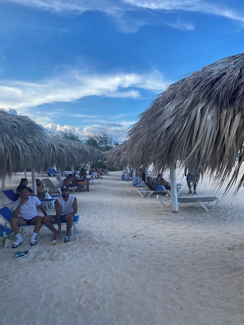 A beach with thatched umbrellas and lounge chairs.