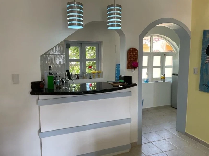 A kitchen with a black countertop, white cabinets, and blue pendant lights. There is a window with a view of greenery outside.