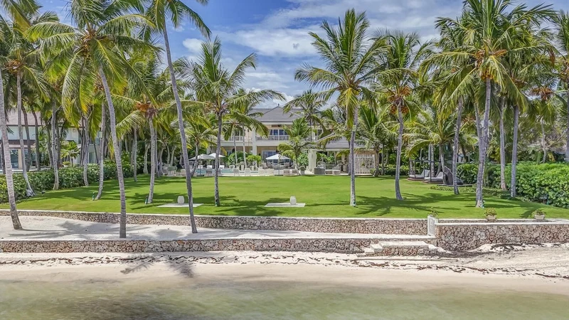 A beachfront resort with palm trees, a swimming pool, and a stone wall.