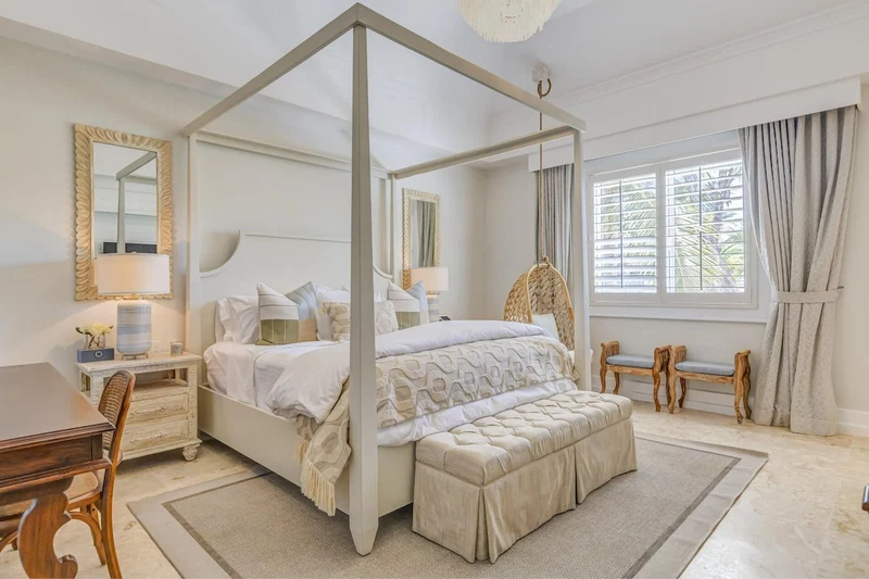 A four-poster canopy bed with a matching bench, a desk with a lamp, and two chairs.