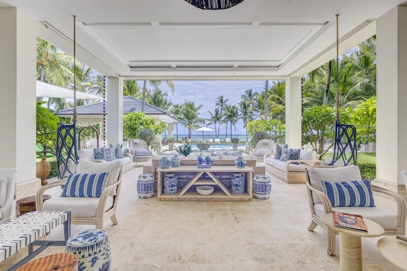 A spacious lounge area with a view of the ocean, furnished with white sofas and blue patterned cushions, and a central coffee table with blue and white decorative items.