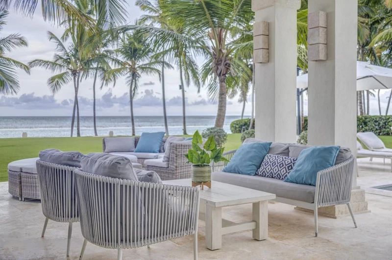 A covered outdoor seating area with wicker furniture, a coffee table, and a view of the ocean.