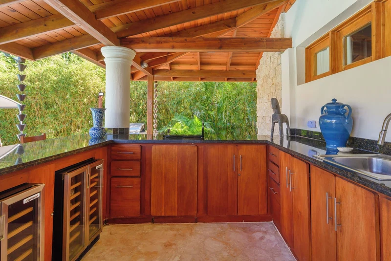 A kitchen with wooden cabinets, a granite countertop, and a view of greenery outside.