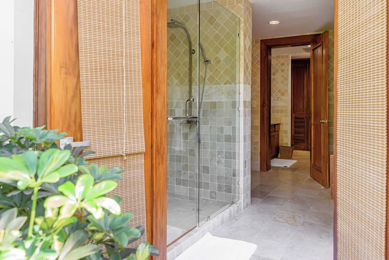 A modern bathroom with a glass-enclosed shower, tiled walls, and a wooden door.